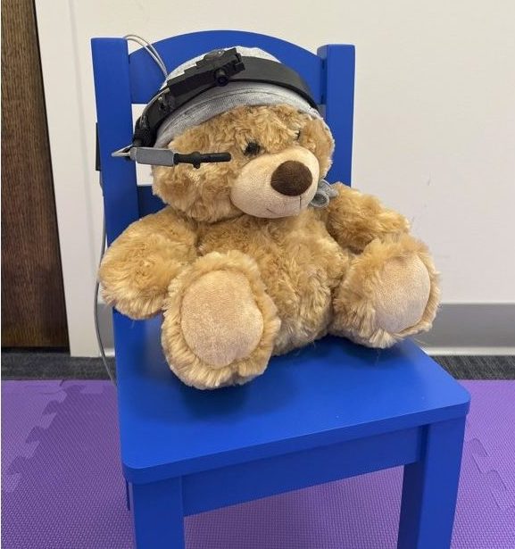 A teddy bear sitting on a blue chair wearing an eye tracking system